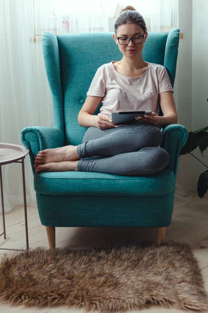 Young woman using a tablet while sitting in a comfortable chairの写真素材