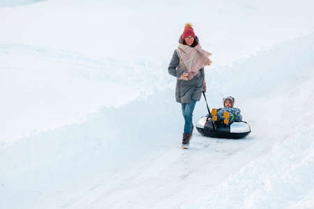 Family mom and child winter activity together on snow tubing on the winter snow roadの写真素材