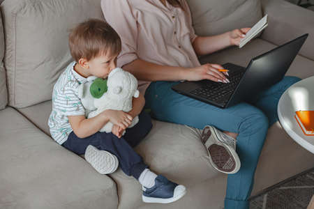 Concept of work at home and home family education, mother working with laptop at home, child playing nearbyの写真素材
