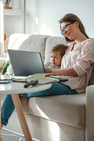 Concept of work at home and home family education, mother working with laptop at home, child playing nearbyの写真素材