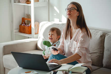 Concept of work at home and home family education, mother working with laptop at home, child playing nearbyの写真素材