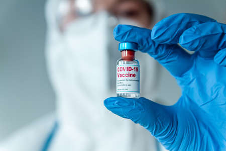 Doctor or nurse in a protective suit holding the covid 19 vaccine in handの写真素材
