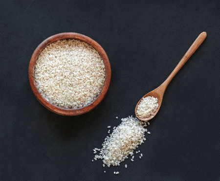 White round rice in a wooden bowl with a wooden or bamboo spoon on black background, top viewの写真素材