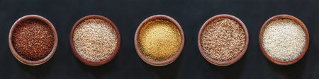 Set of different cereals and rice in wooden bowls on a black background, top view