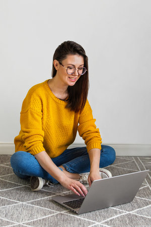 Young woman using laptop sitting on the carpet on white background