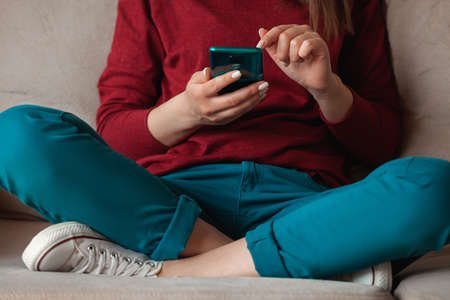 Woman using mobile phone, holding in hands sitting on the sofaの写真素材