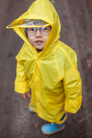 Child in the yellow raincoat walks in the forest and has funの写真素材