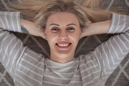Happy young blonde woman lying on carpet, top viewの写真素材
