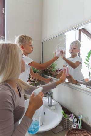 Young mother and son do cleaning together and clean the bathroom mirrorの写真素材