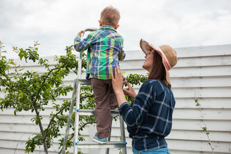 Mother and child on ladder tree, gardening in backyard garden