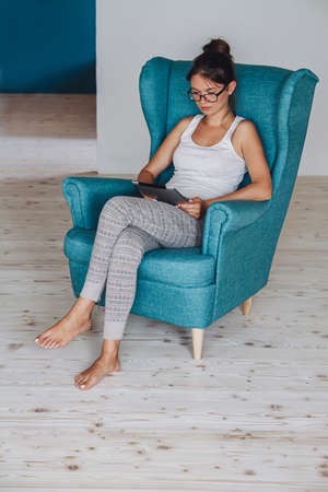 Young woman sitting in armchair and using tablet, isolatedの写真素材