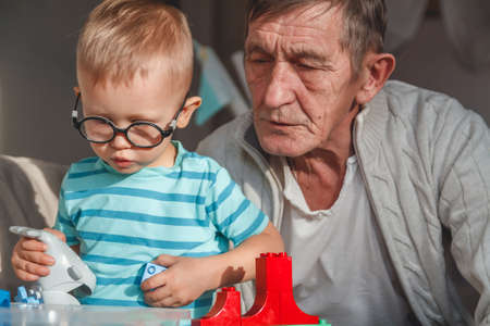 Elderly grandfather plays with little grandson with plastic blocksの写真素材