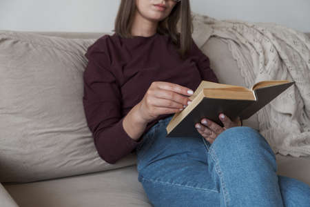 Woman reading book sitting in sofa at homeの写真素材