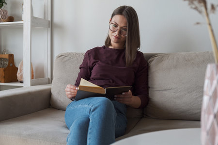 Woman reading book sitting in sofa at home
