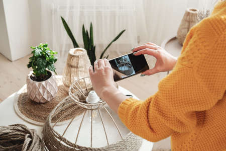 Woman diy blogger takes a photo on a mobile phone for diy blog in social media handmade jute rope lampの写真素材