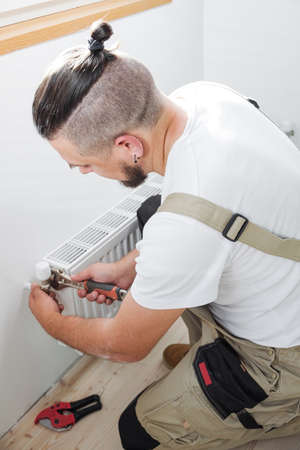 Plumber installing new steel hot water central heating radiatorの写真素材