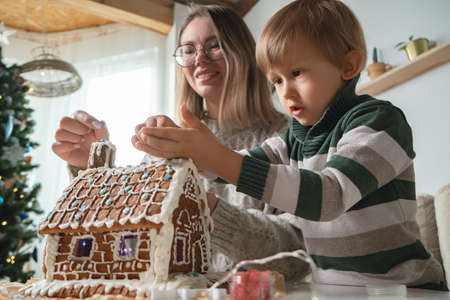 Little boy with mom decorating christmas gingerbread house together, family activities and traditions on Christmas and New Years Eveの写真素材