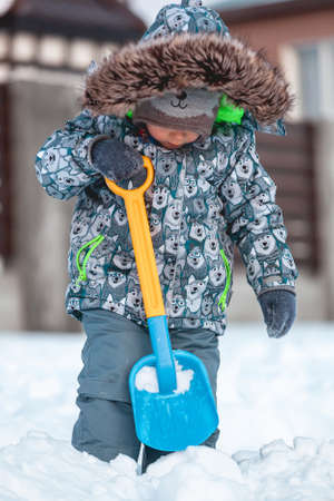 Child playing with shovel on the snow on a sunny winter dayの写真素材