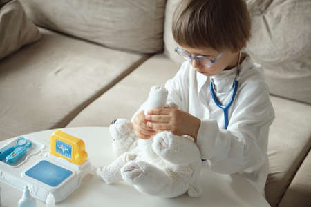 Little doctor in medical coat with stethoscope play bandage to teddy bear toyの写真素材