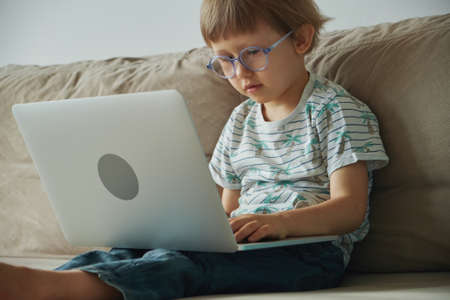 Home schooling, distance learning, Child using laptop while sitting on sofa at homeの写真素材