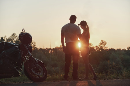 Young beautiful couple motorcyclist hugging at sunset, traveling together on a motorcycleの写真素材