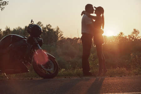 Young beautiful couple motorcyclist hugging at sunset, traveling together on a motorcycleの写真素材