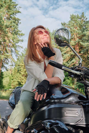 Middle age woman biker drives a motorcycle on a forest road, travels aloneの写真素材