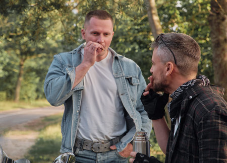 Two man friends of motorcyclists bikers on motorcycles smoking on the side of the road and talking