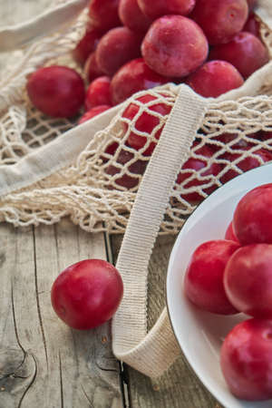 Juicy plums in eco friendly string eco mesh bag on a wooden backgroundの写真素材