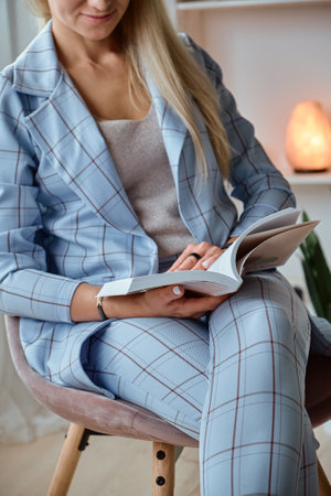 Unrecognizable Young woman in a suit reading a book sitting on a chairの写真素材