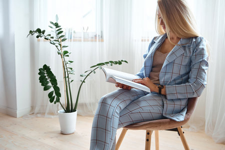Young woman in a suit reading a book sitting on a chairの写真素材