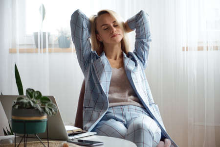 Tired overworked young woman in a suit sitting on a chair in the officeの写真素材