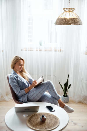 Young woman making notes in notebook sitting at workplace at home, remote workの写真素材