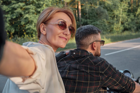 Middle age couple riding a motorcycle having fun and taking selfiesの写真素材