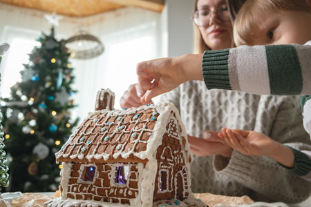 Little boy with mother decorating christmas gingerbread house together, family activities and...