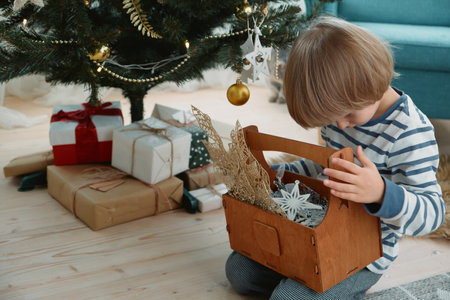 Child decorating a Christmas tree sitting in pajamas in a home interiorの写真素材