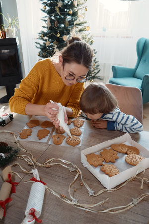 Mother and child decorating Christmas gingerbread cookies with icing sugar togetherの写真素材