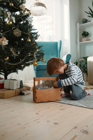 Child decorating a Christmas tree sitting in pajamas in a home interiorの写真素材