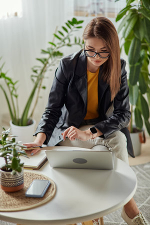 Young woman using laptop and making notes in notebook sitting at workplace at home, remote workの写真素材