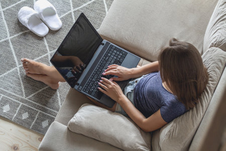 Young woman sitting on sofa and using laptop at homeの写真素材