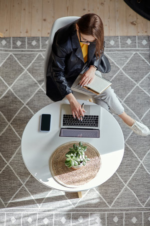 Young woman using laptop and making notes in notebook sitting at workplace at home, remote work top viewの写真素材