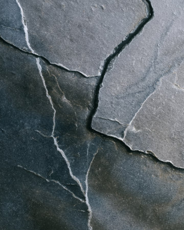 Close-up of natural gray soapstone surface displaying organic crack networks and slate-like texture. A visually rich stone pattern ideal for contemporary use.の素材