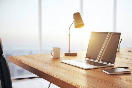 Sunny workplace with wooden desk, laptop, cup of coffee and lamp, on a large window background. 3D Renderingの写真素材