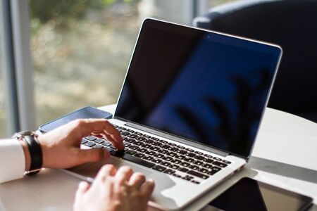 Businessman typing on a laptop keyboard in a sunny office, close upの写真素材