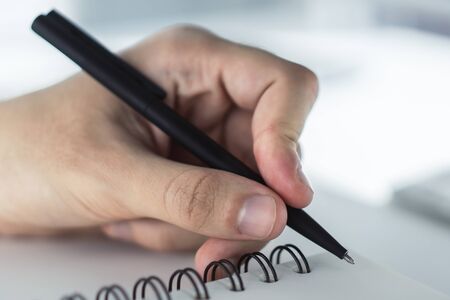 Man writing in notepad. Close up. Focused on a hand with penの写真素材