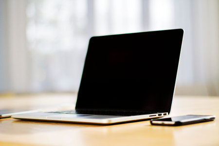 Close up of modern laptop with blank screen on wooden table in sunny interior, mockup. Business and...
