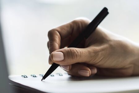 Woman writes with a pen in notepad in a sunny office, business and education concept. Close upの写真素材