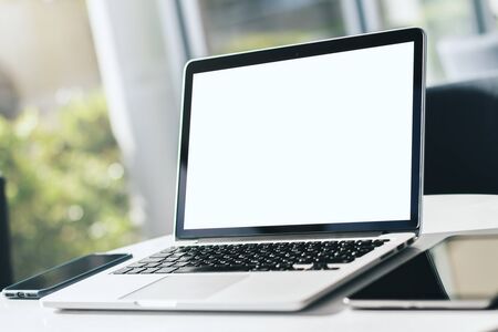 Close up of modern laptop with blank screen on white table in sunny interior, mockup. Business and technology concept