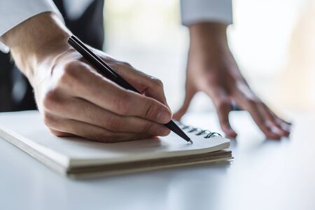 Businessman writes with a pen in diary in a sunny office, business and education concept. Close upの写真素材