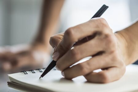 Businesswoman writes with a pen in diary in a sunny office, business and education concept. Close upの写真素材